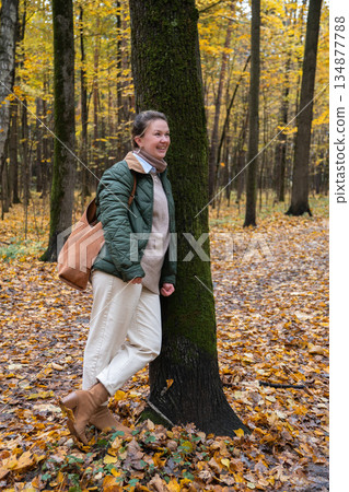 Smiling woman stands by mossy tree in Timiryazevsky Park, Moscow, surrounded by yellow autumn leaves and a calm forest mood Smiling woman stands by mossy tree in Timiryazevsky Park, Moscow, surrounded by yellow autumn leaves and a calm forest mood 134877788