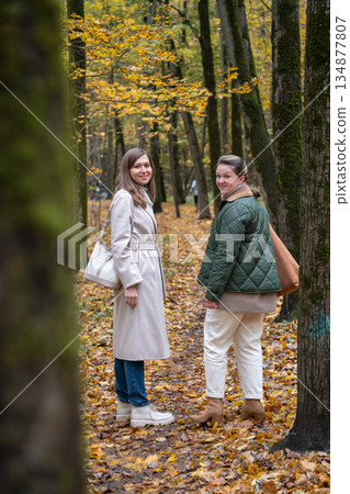 Two women standing and talking on a forest path during autumn in Timiryazevsky Park, Moscow, surrounded by yellow leaves and tall trees Two women standing and talking on a forest path during autumn in Timiryazevsky Park, Moscow, surrounded by yellow leaves and tall trees 134877807