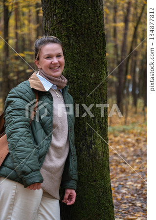 Smiling woman stands by mossy tree in Timiryazevsky Park, Moscow, surrounded by yellow autumn leaves and a calm forest mood 134877812