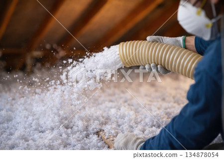 Worker Blowing Insulation Material into Attic During Home Energy Upgrade 134878054