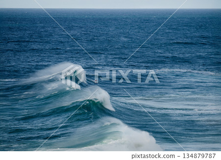 Surfer rides towering blue wave in open ocean, dynamic sea spray and powerful motion 134879787