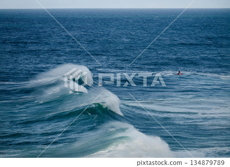 Powerful ocean waves crash as surfers ride towering swells under a clear blue sky Powerful ocean waves crash as surfers ride towering swells under a clear blue sky 134879789