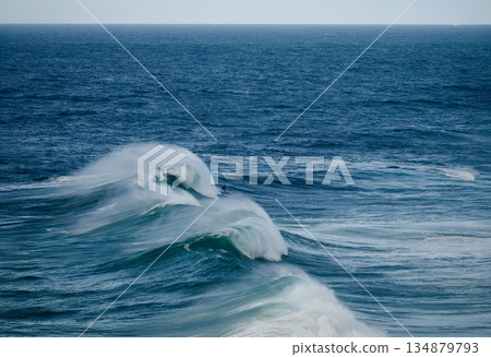 Powerful ocean waves with surfers riding a breaking barrel under a clear blue sky 134879793