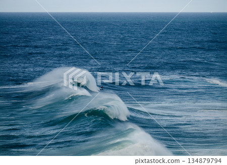 Surfers ride powerful ocean waves as tall curling swells crash in deep blue sea Surfers ride powerful ocean waves as tall curling swells crash in deep blue sea 134879794