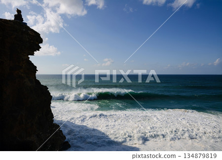 Person on a cliff overlooking the ocean with waves crashing against the rocky shore 134879819