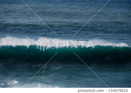 A powerful ocean wave rolls toward the shore with deep blue and green hues A powerful ocean wave rolls toward the shore with deep blue and green hues 134879828