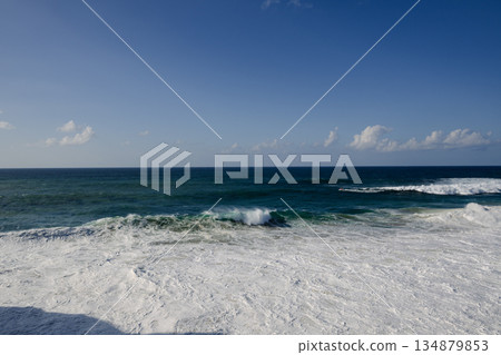 Serene ocean scene with blue sky, gentle waves and white foam on a sunny beach Serene ocean scene with blue sky, gentle waves and white foam on a sunny beach 134879853