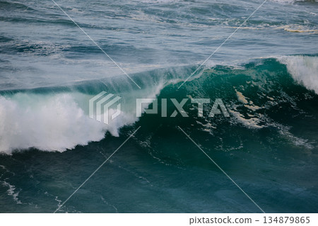 Powerful ocean wave curling toward the shore with turquoise water, white foam, and spray 134879865
