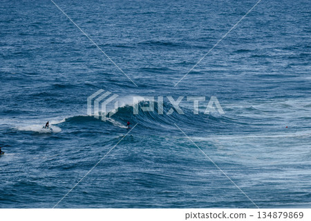 Surfers ride a powerful blue ocean wave, capturing intense motion and sport in the open sea 134879869