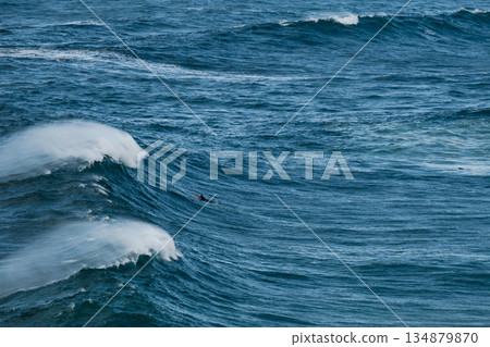 Surfer riding a massive ocean wave in deep blue sea during a windy day Surfer riding a massive ocean wave in deep blue sea during a windy day 134879870