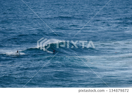 Surfers riding large ocean waves in a bright blue sea, capturing action and adventure Surfers riding large ocean waves in a bright blue sea, capturing action and adventure 134879872