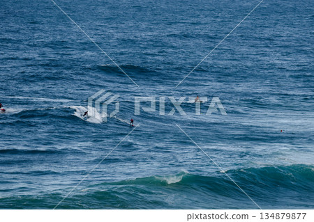Surfers ride large blue ocean waves in an energetic open-sea scene of sport and motion Surfers ride large blue ocean waves in an energetic open-sea scene of sport and motion 134879877