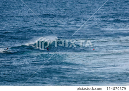 Surfers ride a powerful ocean wave as rugged blue water glides beneath the cresting swell 134879879