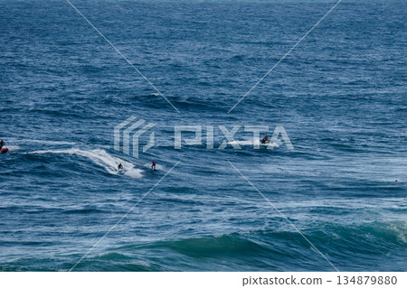 Surfers riding large ocean waves, multiple riders carving white water across the open sea 134879880