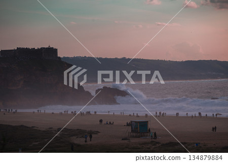 Evening on the beach with waves, cliffs, and a fortress overlooking a busy shoreline 134879884
