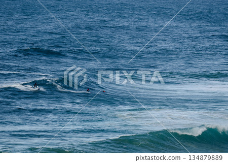 Surfers riding large ocean waves together, distant riders in turquoise sea 134879889