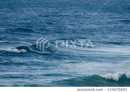 Surfers ride large ocean waves with several surfers paddling and waiting in blue sea Surfers ride large ocean waves with several surfers paddling and waiting in blue sea 134879893