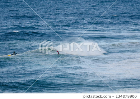 Two surfers ride a powerful wave as the ocean roars under a clear blue sky Two surfers ride a powerful wave as the ocean roars under a clear blue sky 134879900