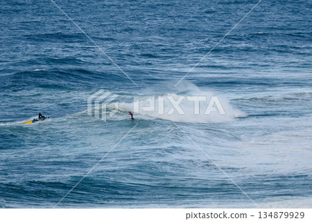 Surfers ride a powerful ocean wave as curling white spray crashes nearby 134879929