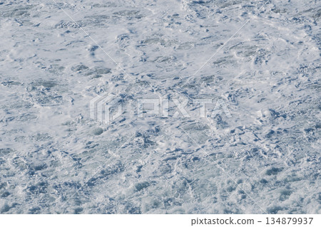 Rough sea foam covers the icy ocean surface, creating a cold, dynamic coastal scene 134879937