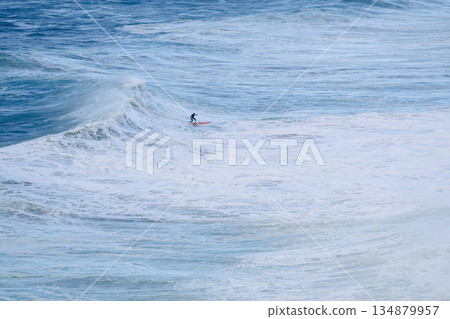Surfer riding a massive ocean wave on a bright red board in a vast blue seascape Surfer riding a massive ocean wave on a bright red board in a vast blue seascape 134879957