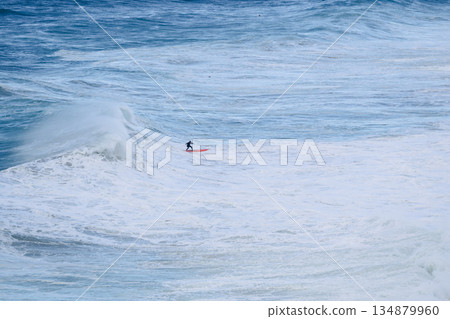 Surfer rides a dramatic big wave on a red board in the open blue ocean 134879960