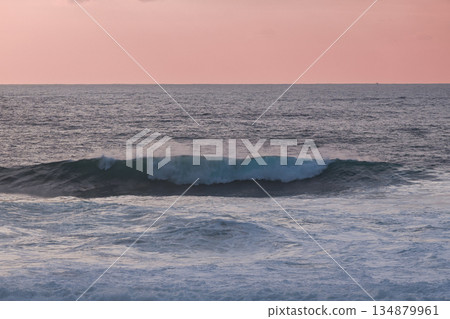 Calm ocean waves roll under a pink sunset sky over the tranquil sea Calm ocean waves roll under a pink sunset sky over the tranquil sea 134879961