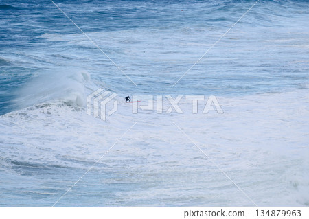 Surfer riding a massive ocean wave on a bright day for dramatic seascape and action 134879963