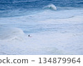 Surfer rides a massive wave in rough ocean conditions on a bright red board 134879964