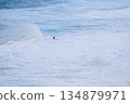 Surfer riding a towering ocean wave on a red board under blue sky and white spray 134879971