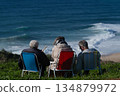 Three people sit in colorful beach chairs facing the ocean, enjoying a peaceful coastal moment 134879972