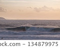 Calm ocean sunset with large waves and distant coastline, surfers nearby 134879975