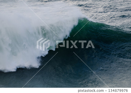 Massive ocean wave curling and breaking with white spray over deep blue water Massive ocean wave curling and breaking with white spray over deep blue water 134879976