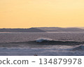 Golden hour ocean waves roll toward distant coast under warm orange sunset sky 134879978