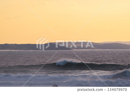 Golden hour ocean waves roll toward distant coast under warm orange sunset sky Golden hour ocean waves roll toward distant coast under warm orange sunset sky 134879978