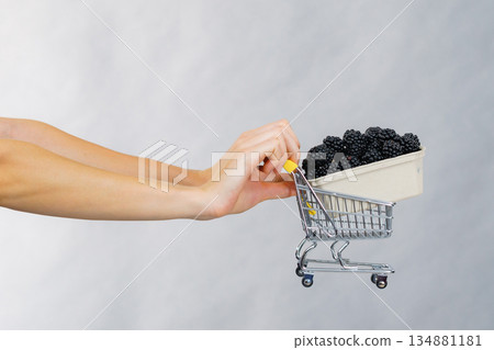 Hand holds blackberry fruits in shopping cart Hand holds blackberry fruits in shopping cart 134881181