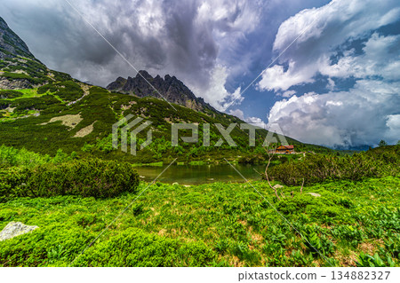 Traditional mountain hut by a lake under a dramatic stormy sky 134882327