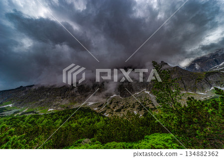 Dramatic storm clouds and mist covering mountain peaks Dramatic storm clouds and mist covering mountain peaks 134882362