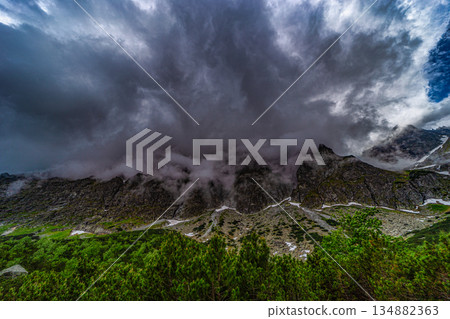 Dramatic storm clouds and mist covering mountain peaks Dramatic storm clouds and mist covering mountain peaks 134882363