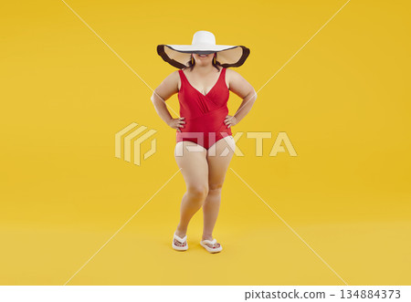 Funny fat woman in swimsuit and big beach hat isolated on studio yellow background. Funny fat woman in swimsuit and big beach hat isolated on studio yellow background. 134884373
