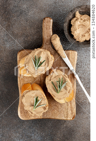 Toasted baguette slices with chicken liver pate and rosemary on rustic background. Top view. Copy space. Toasted baguette slices with chicken liver pate and rosemary on rustic background. Top view. Copy space. 134884620
