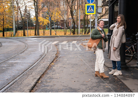 Two women talk and laugh near historic wooden tram stop in Moscow, with wet pavement, tram tracks, street signs, autumn trees in the city background 134884897