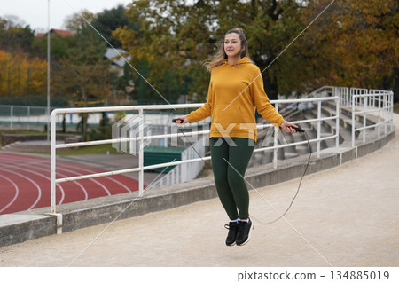 A woman in a yellow hoodie jumps rope at a stadium A woman in a yellow hoodie jumps rope at a stadium 134885019
