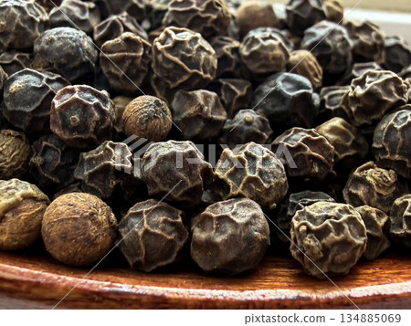 Macro Close-Up of Whole Black Peppercorns on Wooden Spoon Culinary Spice Background 134885069