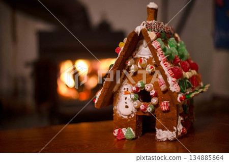 Gingerbread house with candy decoration by cozy fireplace 134885864