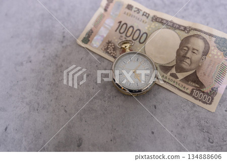 一張皺巴巴的10000日元鈔票和一塊懷錶-時間即金錢的意象。 一張皺巴巴的10000日元鈔票和一塊懷錶-時間即金錢的意象。 134888606