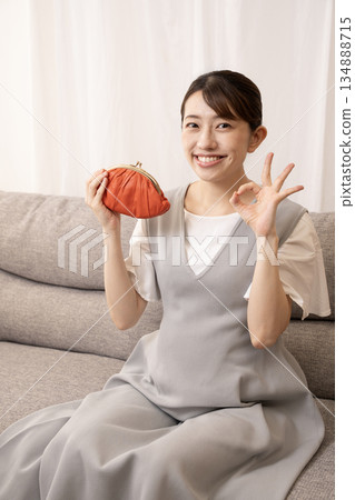 An eight-month pregnant woman sitting on a sofa and holding a red wallet An eight-month pregnant woman sitting on a sofa and holding a red wallet 134888715