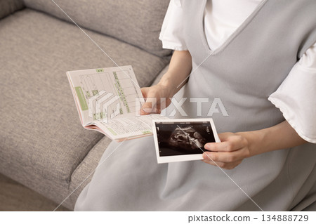 A pregnant woman holding her maternal and child health handbook and ultrasound images. A pregnant woman holding her maternal and child health handbook and ultrasound images. 134888729
