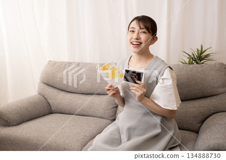 A pregnant woman sitting on a sofa and holding a maternal and child health handbook and an ultrasound photo 134888730