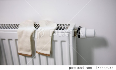 White socks drying on a radiator during the seasonal heating period. Concept of wintertime home heating, energy consumption, warmth, comfort, and everyday life in cold seasons. White socks drying on a radiator during the seasonal heating period. Concept of wintertime home heating, energy consumption, warmth, comfort, and everyday life in cold seasons. 134888932